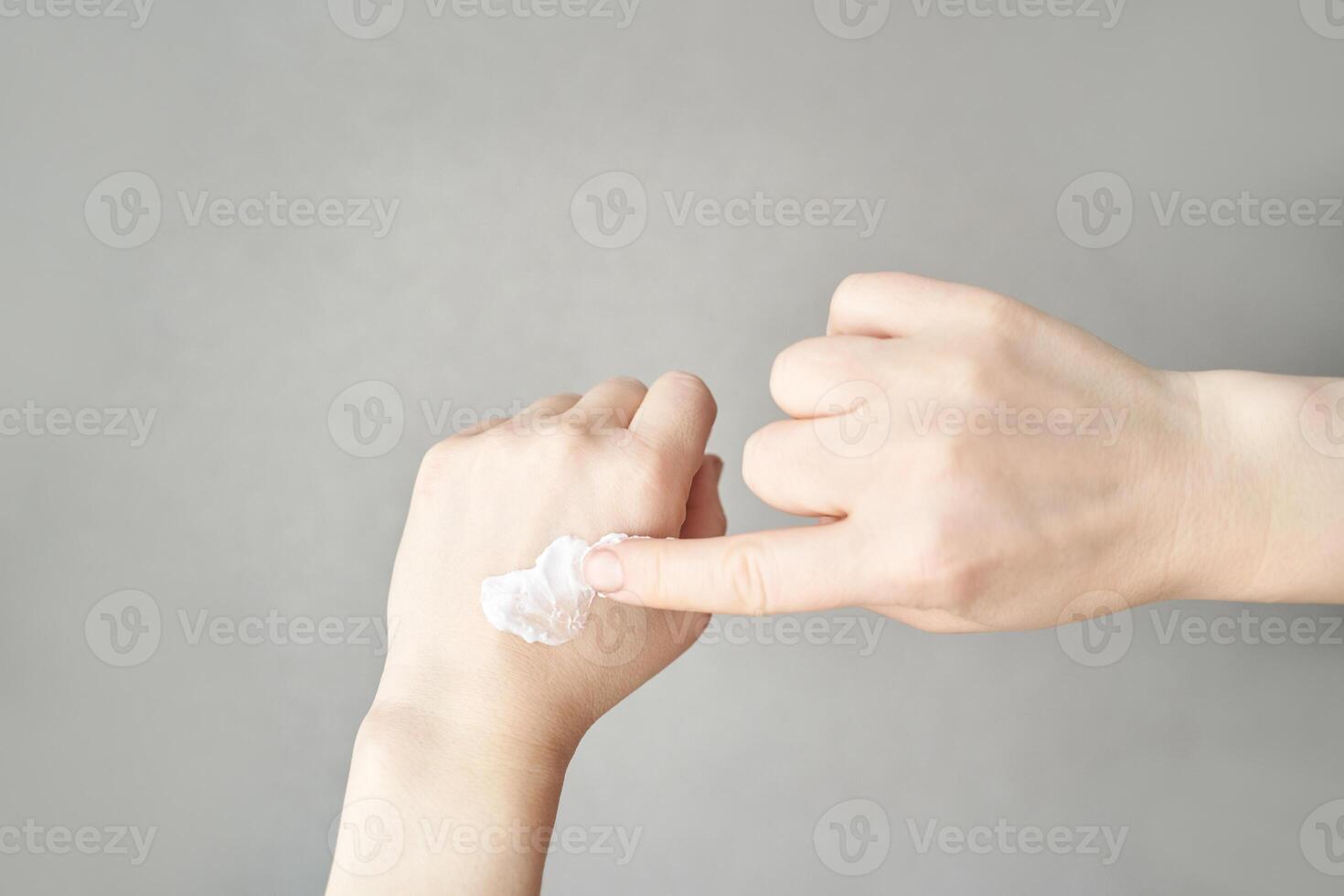 Young caucasian female applying skincare cream to hand for moisturizing and hydration against gray background. photo