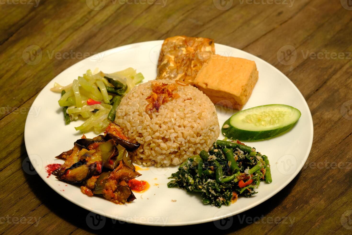 Nasi Campur Vegetarian is is brown rice with sauted green vegetables, sambal, fresh cucumber and tomato slices, fried tofu, and fried tempeh. Suitable for vegetarians. Indonesian food. Nasi Rames. photo