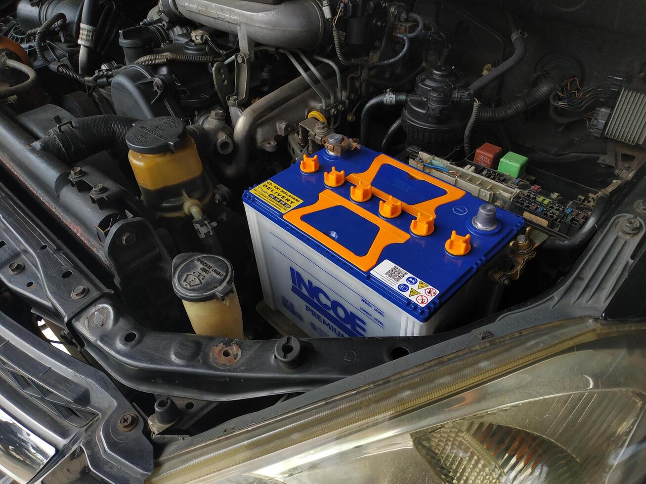 Banyumas, Indonesia - November 26 2024, An open car hood displays a prominently placed blue and orange battery, showcasing automotive components and maintenance details. photo