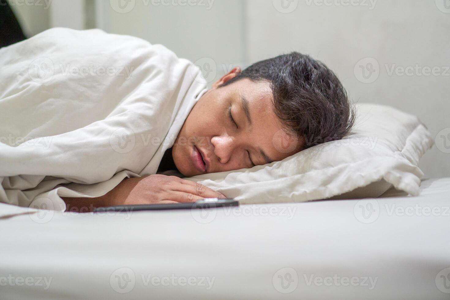 Asian man using white shirt sleeping in bed. Tired, fatigue and relax male lying his head on the pillow. Peacefulness concept. photo