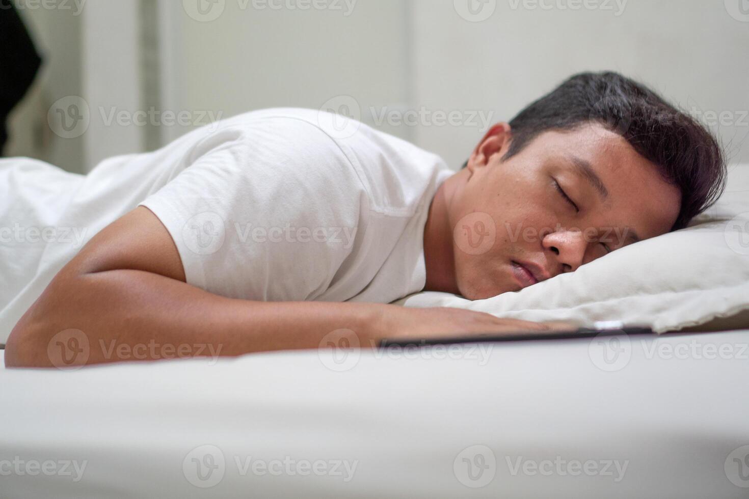 Asian man using white shirt sleeping in bed. Tired, fatigue and relax male lying his head on the pillow. Peacefulness concept. photo