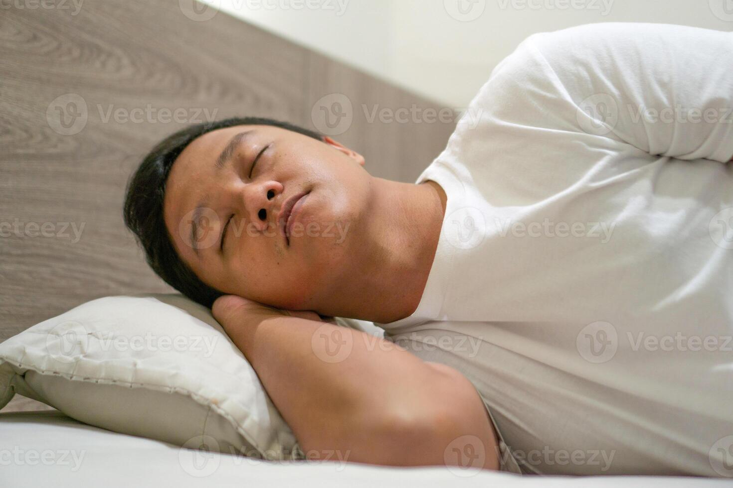 Asian man using white shirt sleeping in bed. Tired, fatigue and relax male lying his head on the pillow. Peacefulness concept. photo
