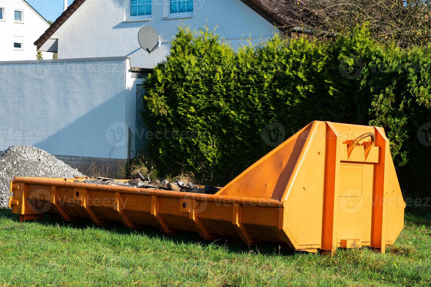 Construction debris container placed in a grassy area near buildings photo