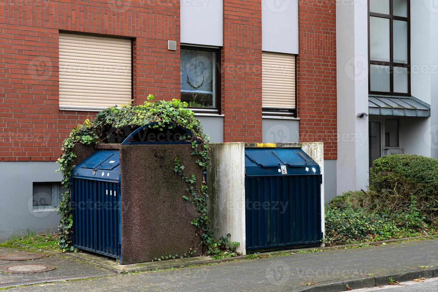 Two recycling bins covered in green foliage beside a building photo