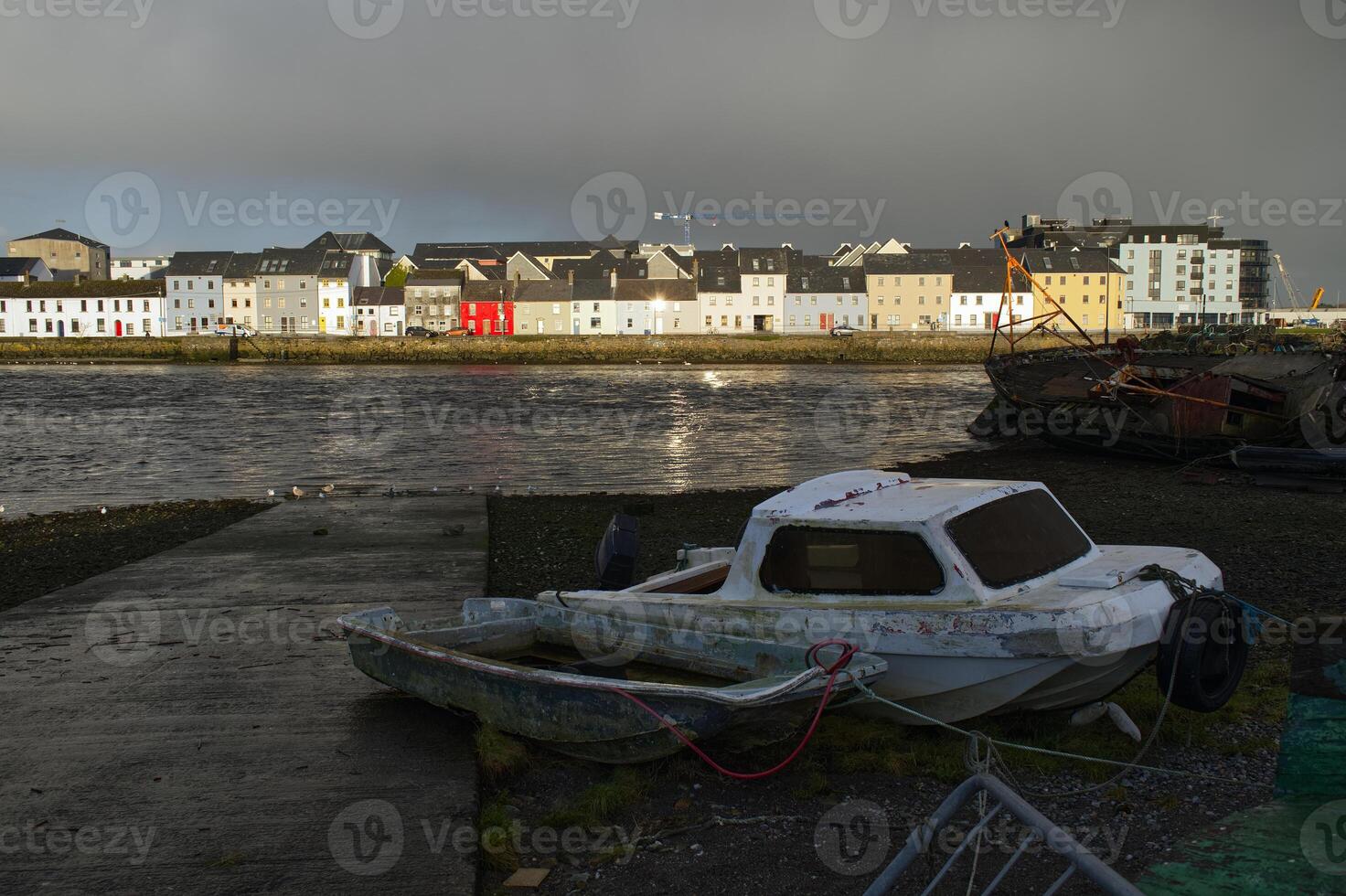 Cloudy cityscape sunrise scenery with old wooden boat in Corrib river at Claddagh in Galway city, Ireland, architecture background photo