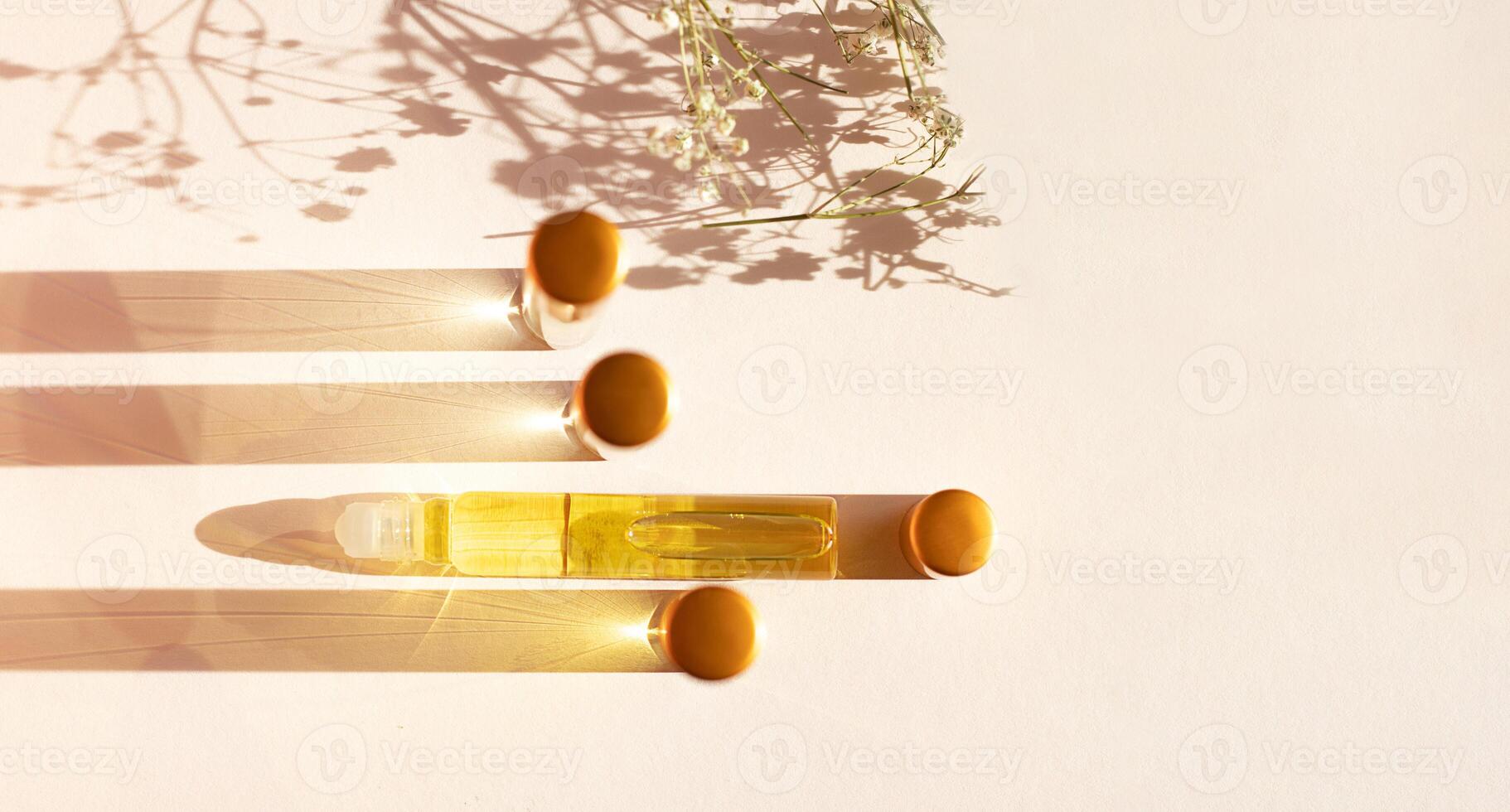 Oil perfume in travel bottles on a beige background with copy space, shadow from flowers photo