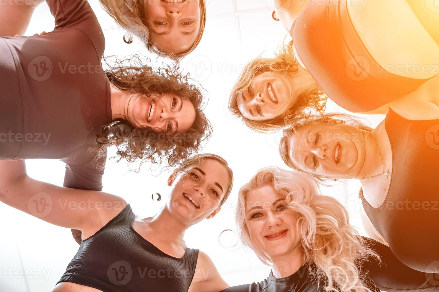 Low angle shot of smiling women looking at the camera, hugging, standing in a circle and doing team building photo