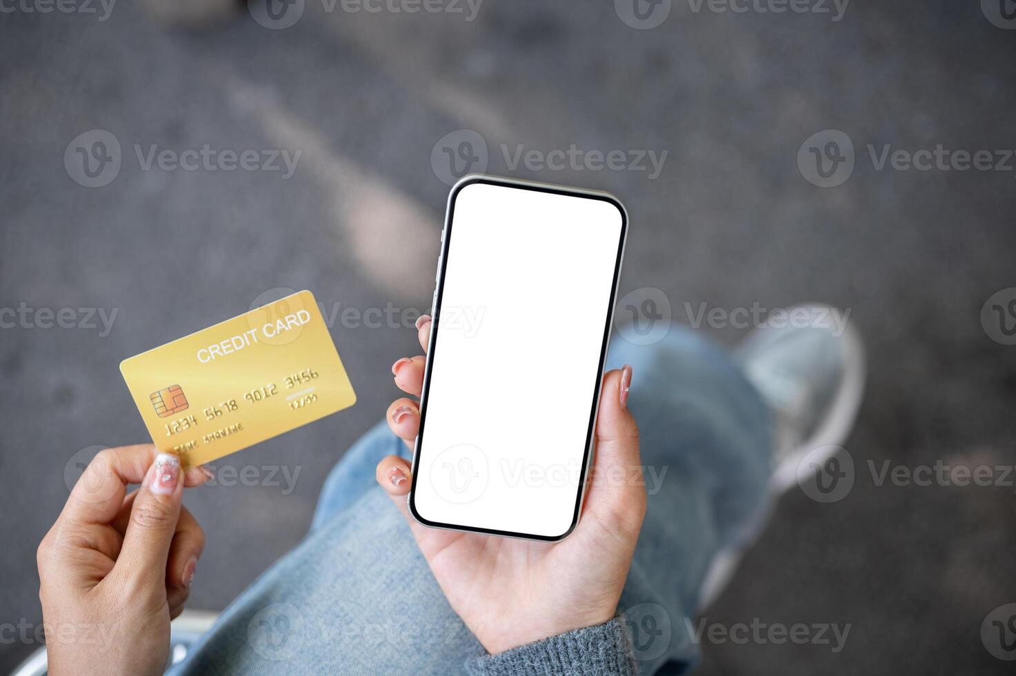 A top view of a woman sitting outdoors, holding a credit card and a smartphone with a screen mockup. photo