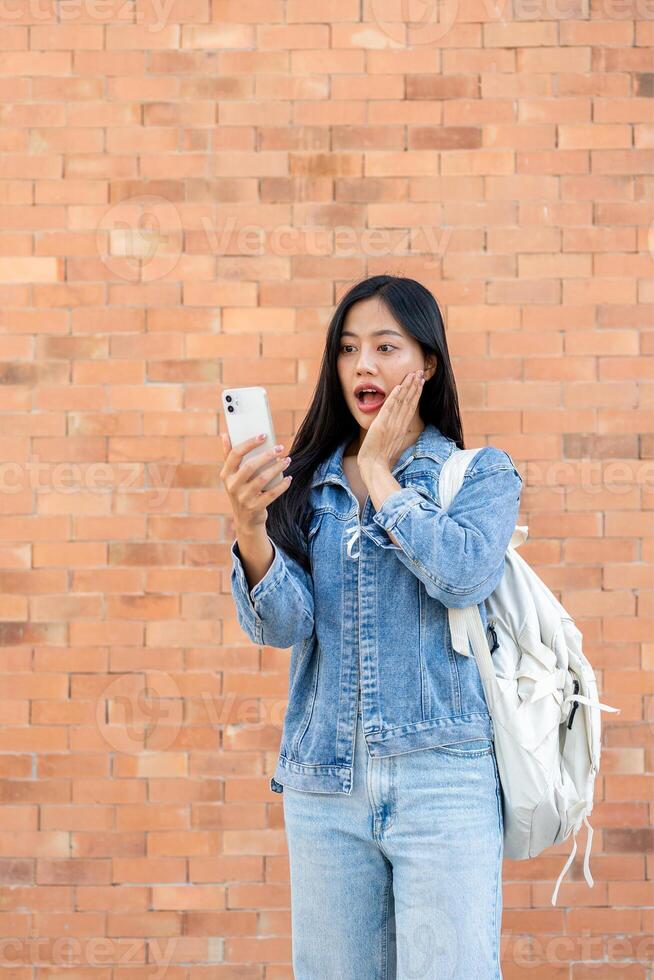 An amazed Asian female college student looking at her smartphone screen with a surprised expression. photo