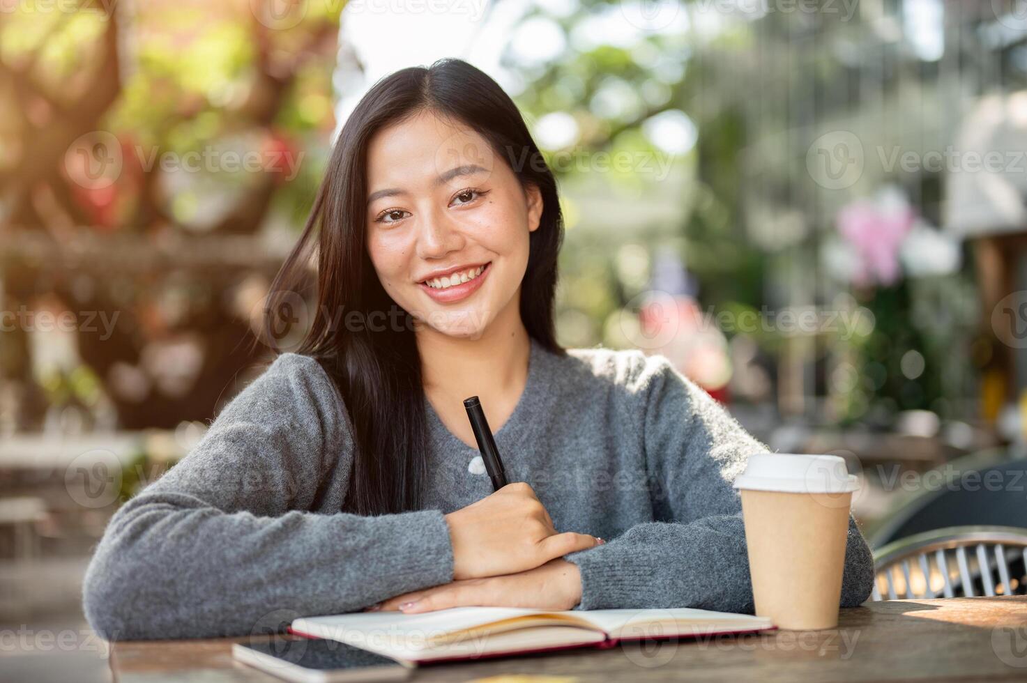 A beautiful, positive Asian woman sits at an outdoor cafe table, writing in a book or diary. photo