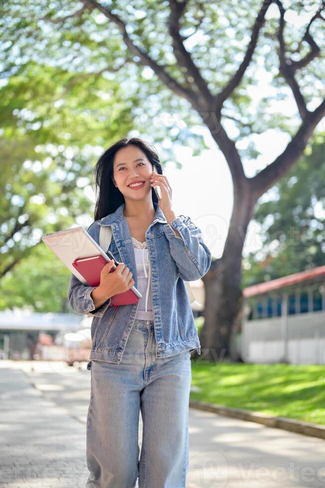 A cheerful female student enjoys talking on the phone with her friend while on her way to class. photo