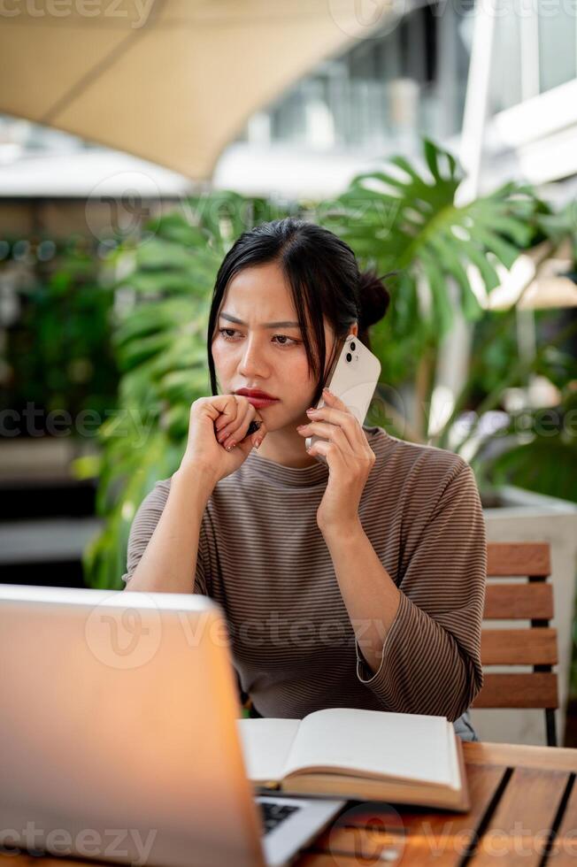 A thoughtful Asian woman is having a serious conversation on the phone, working remotely from a cafe photo