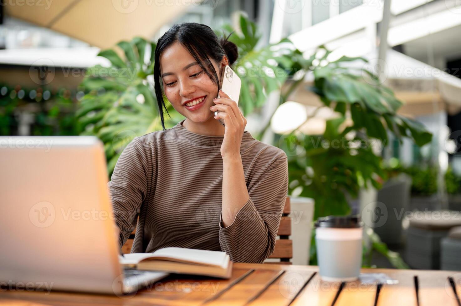 A beautiful Asian woman talking on the phone while working remotely from a cafe. photo