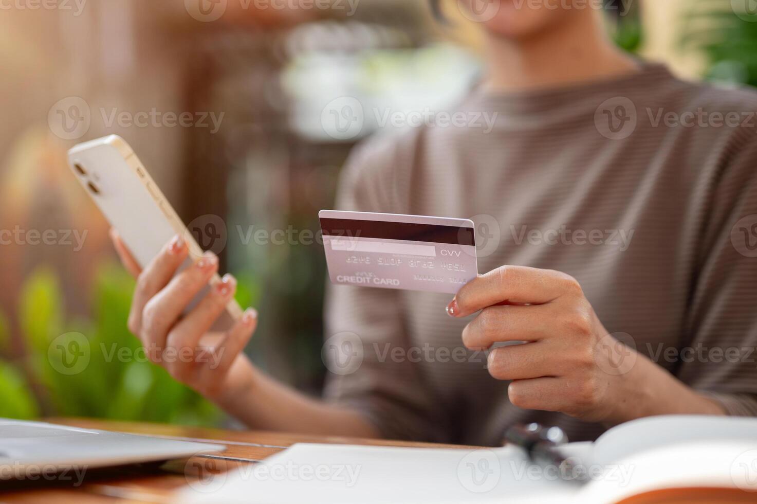 A woman holding a credit card and a smartphone while sitting at an outdoor table of a cafe. photo