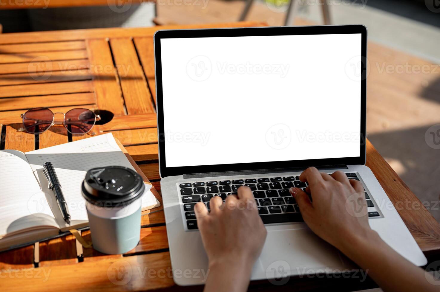 A woman typing on laptop keyboard while sitting at an outdoor table of a coffee shop on a sunny day photo