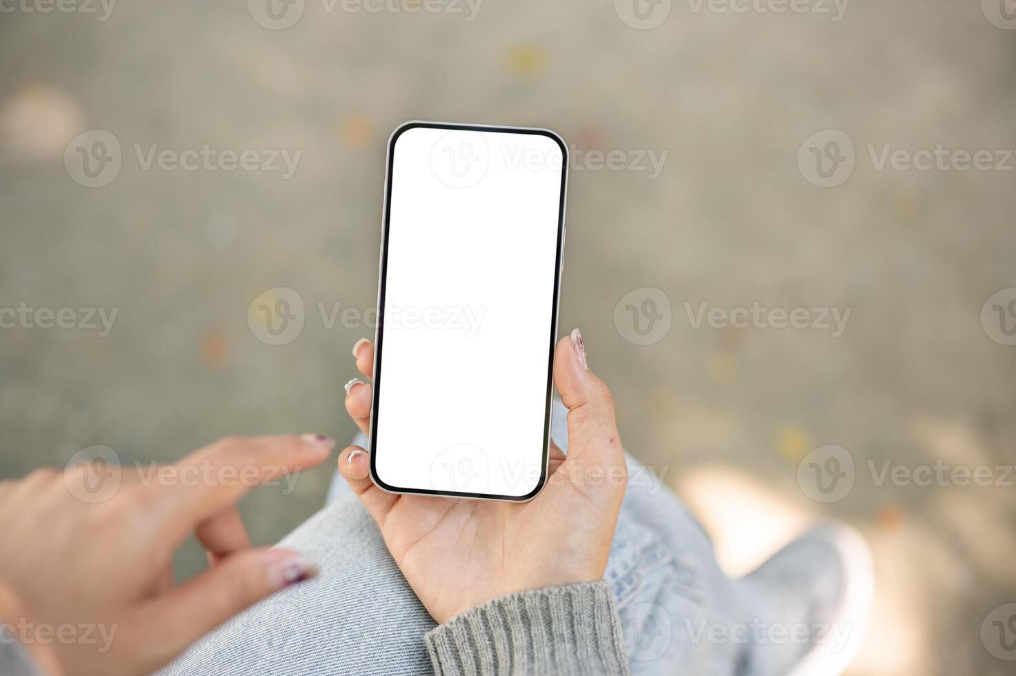 A close-up of a woman sitting outdoors in a park, using her smartphone, touching the screen. photo