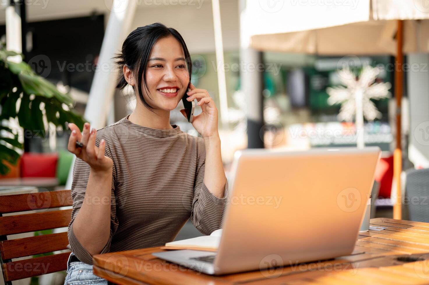 A beautiful Asian woman talking on the phone while working remotely from a cafe. photo