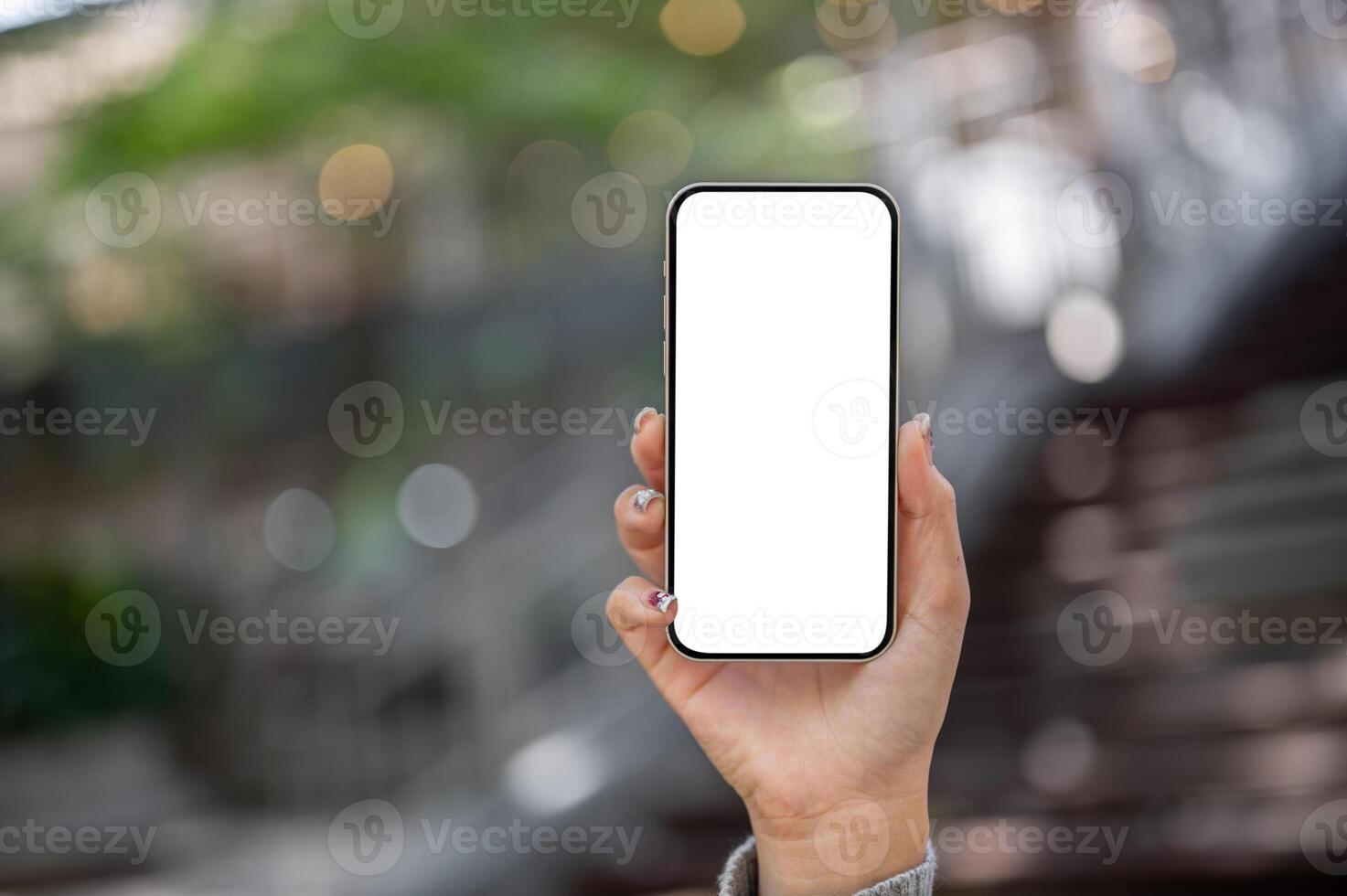 A woman's hand holding a smartphone with a white screen mockup, showing it toward the camera. photo