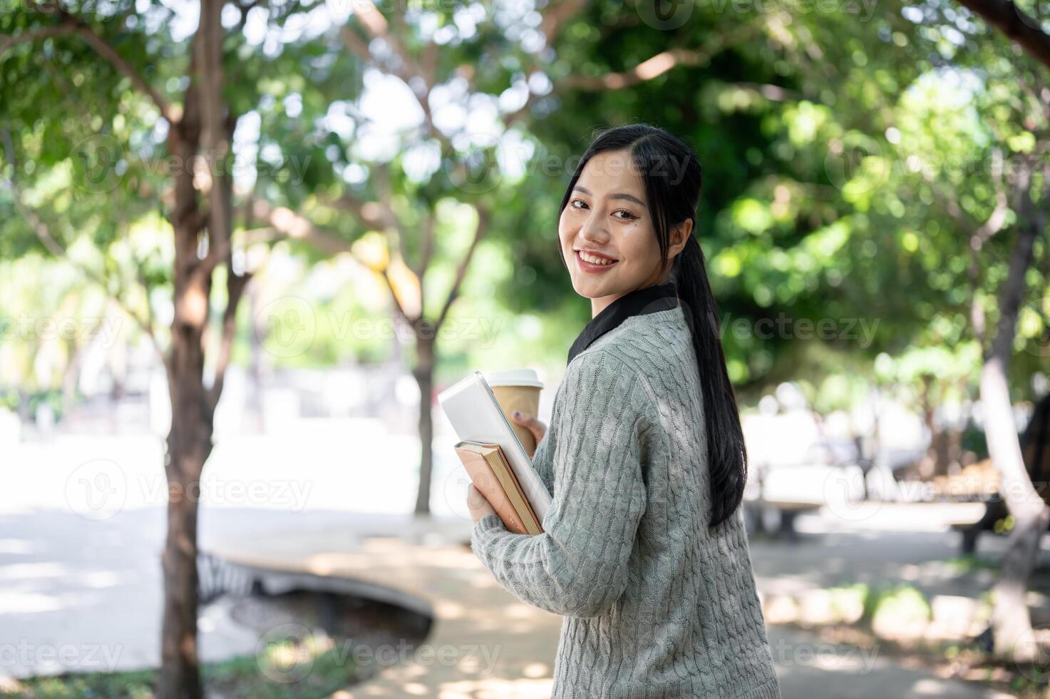 A charming, happy Asian female college student walks along the footpath on campus on a bright day. photo