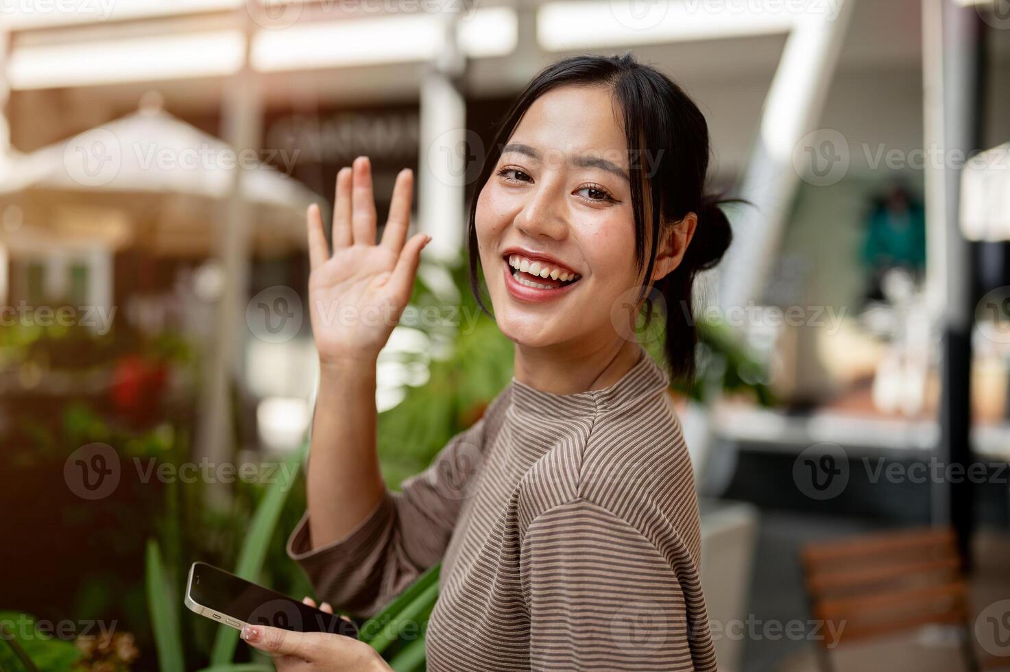 A beautiful, positive Asian woman stands outdoors with a smartphone and smiles at the camera. photo