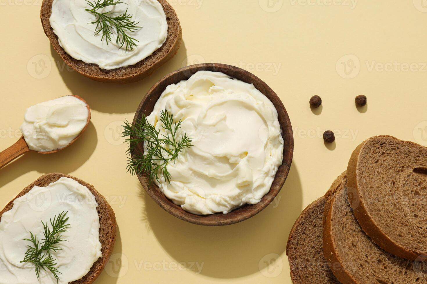 Philadelphia cheese in a wooden plate and with sandwiches on a yellow background. photo