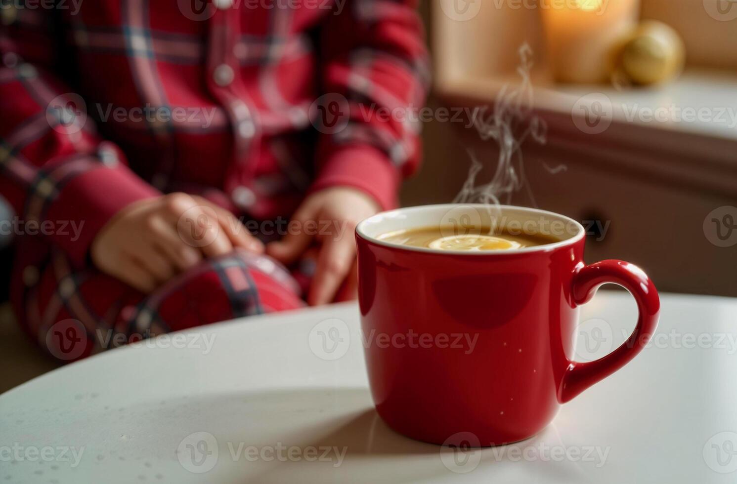 A red mug with a hot healing drink topped with a lemon slice, blurred person wearing red plaid pajamas in the background, warm cozy evening interior photo