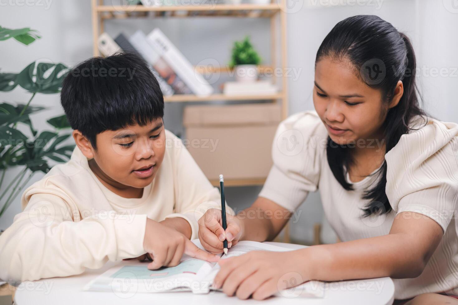 Teacher or sister helping boy writing lesson and learning to write, Female tutor helping little elementary school boy with homework during individual lesson at home photo