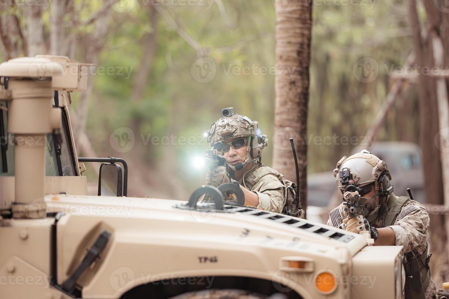 Soldiers in camouflage uniforms hold weapons ready to fire, By hiding on the side military communication vehicle photo