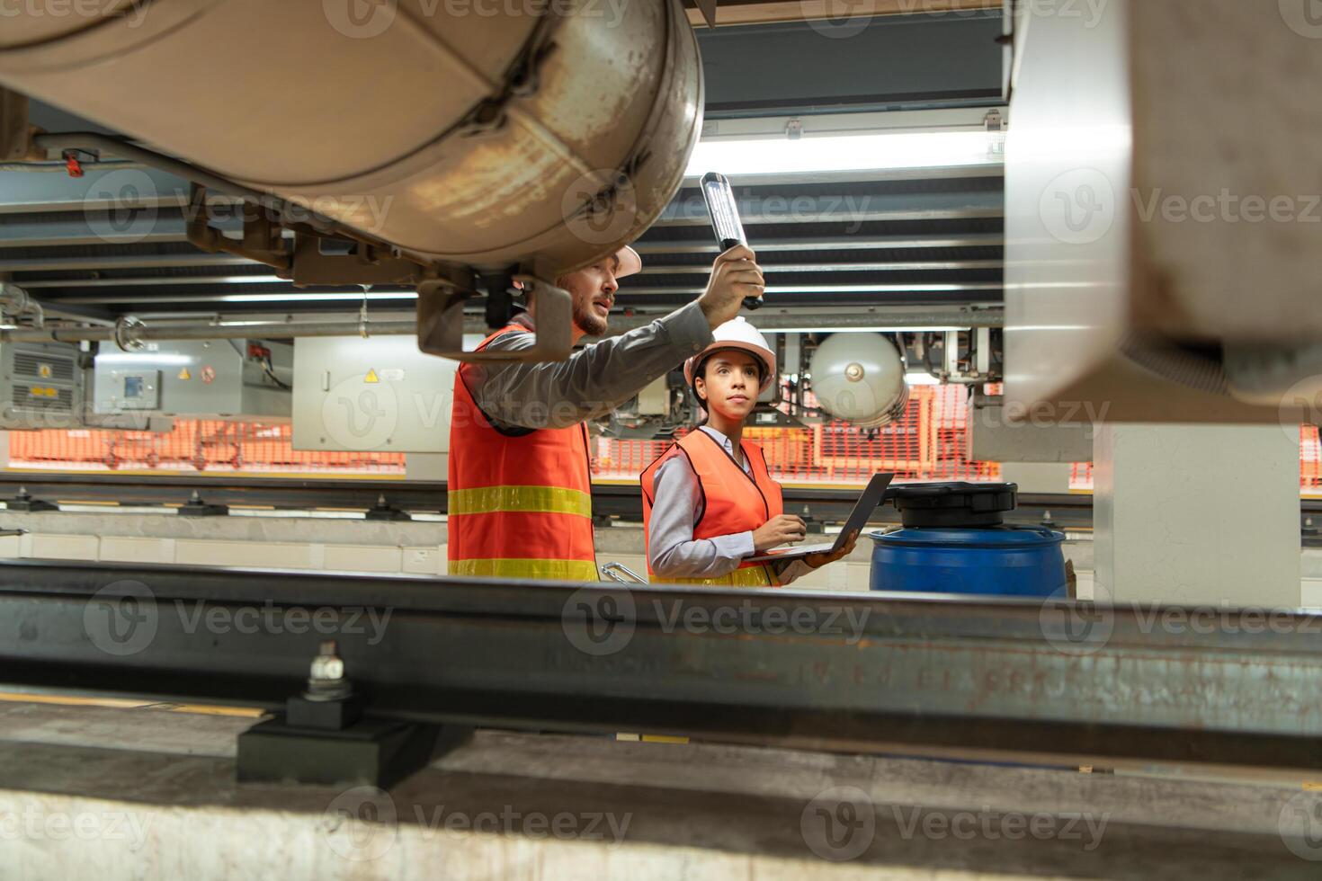 Male and female engineers work together in an electric repair station. Inspecting the undercarriage of electric train that are being repaired at the garage. photo