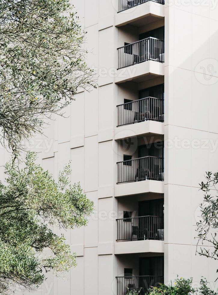 A modern apartment building with a minimalist facade featuring multiple balconies with black metal railings photo