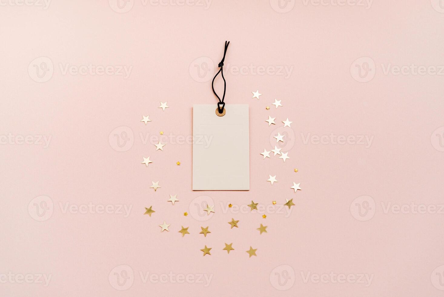 White tag with a black string is placed in the center, surrounded by gold star-shaped decorations on a soft beige background. photo