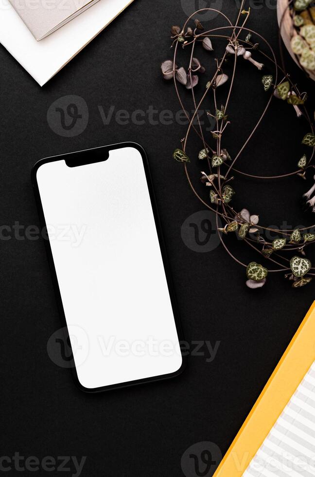 Modern smartphone on black table background with fragile houseplant and notepads photo