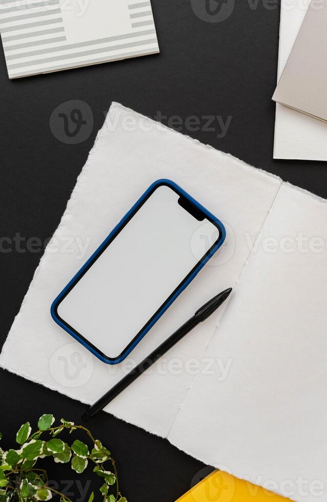 Modern smartphone with blue case on open notepad on black table background with green houseplant decoration photo