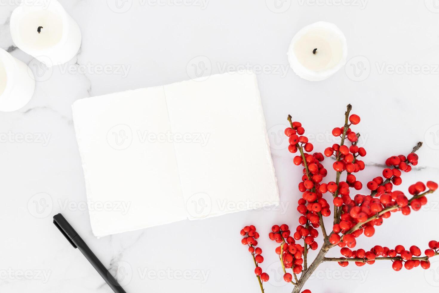 Minimal Christmas decorations candles and branch with red berries and open blank notebook on white marble table background. photo
