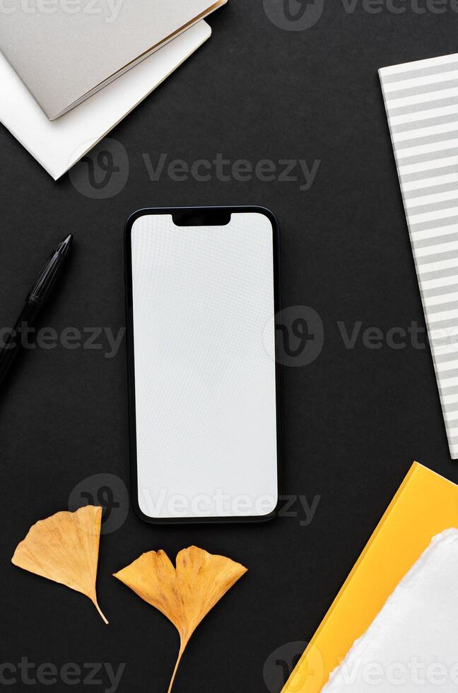 Modern smartphone on black table background with nature decoration, yellow and gray notepads photo