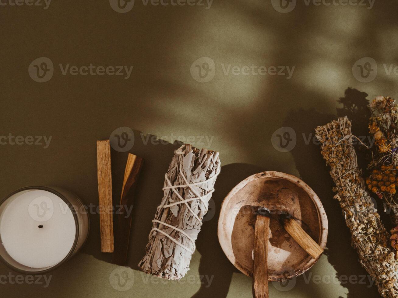 Items for spiritual cleansing - sage and flowers bundle, palo santo incense sticks, white candle on green background. photo