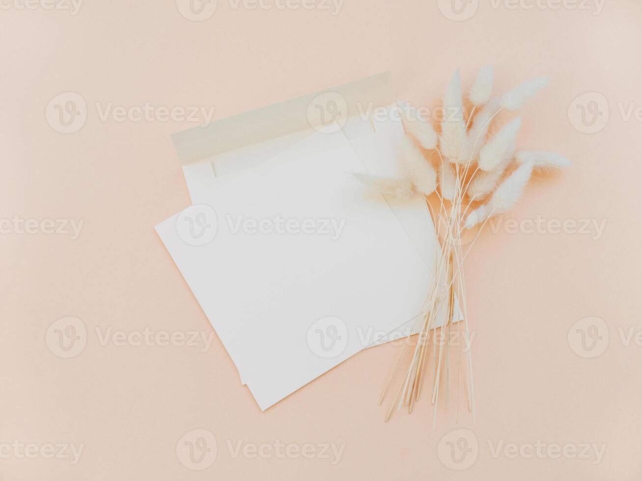 White blank card for text and envelope next to bouquet of dry Lagurus on beige background. photo