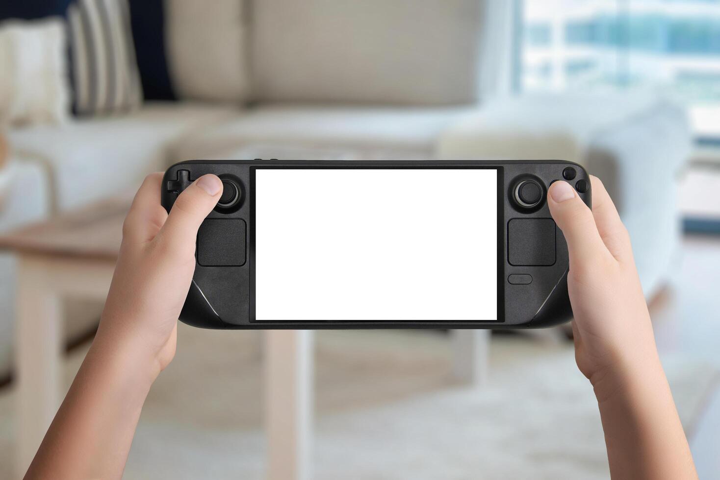 Flat lay or front view of hands holding a black handheld gaming console with isolated screen, cozy living room background, ideal for mockup game presentation and design photo