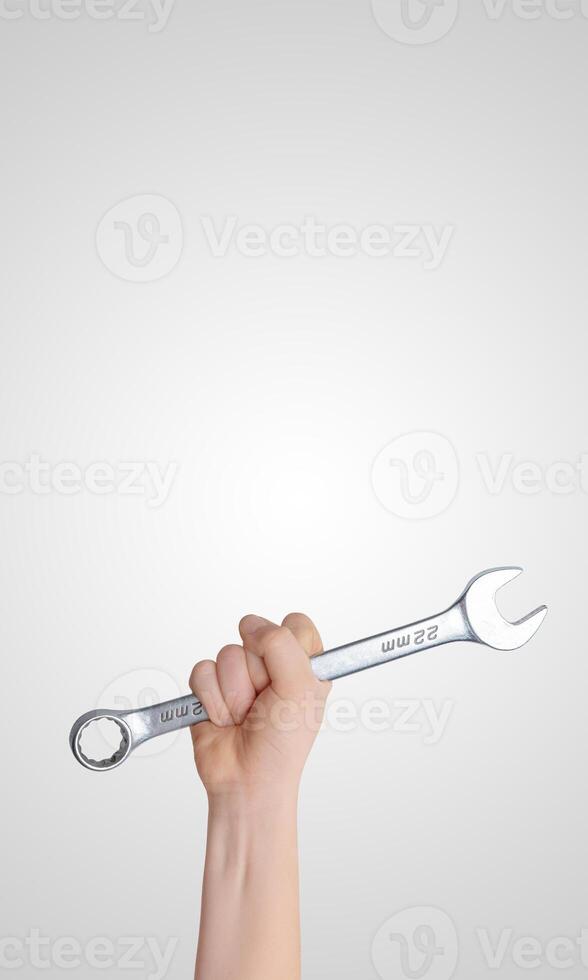 Hand holding a wrench raised high against a gray background, vertical composition with free space for promotional text, ideal for tool branding or industrial concept photo