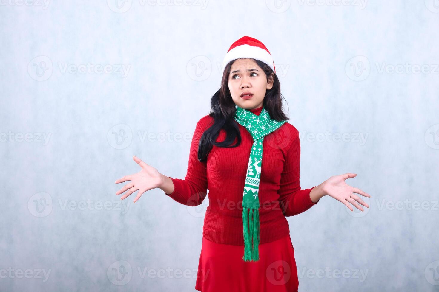 girl expression wearing red sweater party wear with Santa hat and scarf celebrating christmas and new year, both hands open to the side surprised hesitant look right, isolated on white background photo