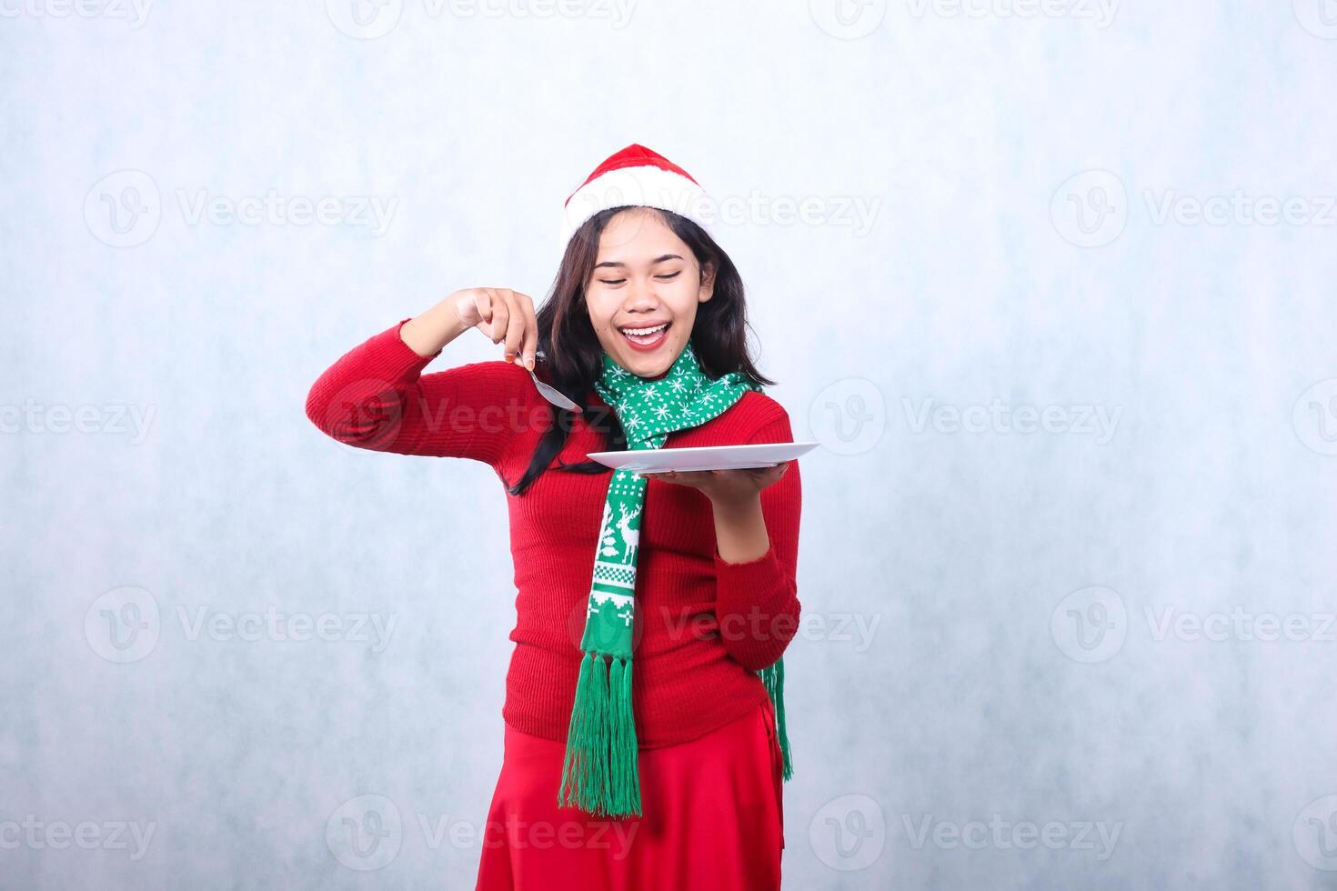 portrait of woman wearing red sweater red sweater with santa hat and scarf celebrating merry christmas and new year, cheerful to food carry white plate and hold spoon ,isolated on white background photo