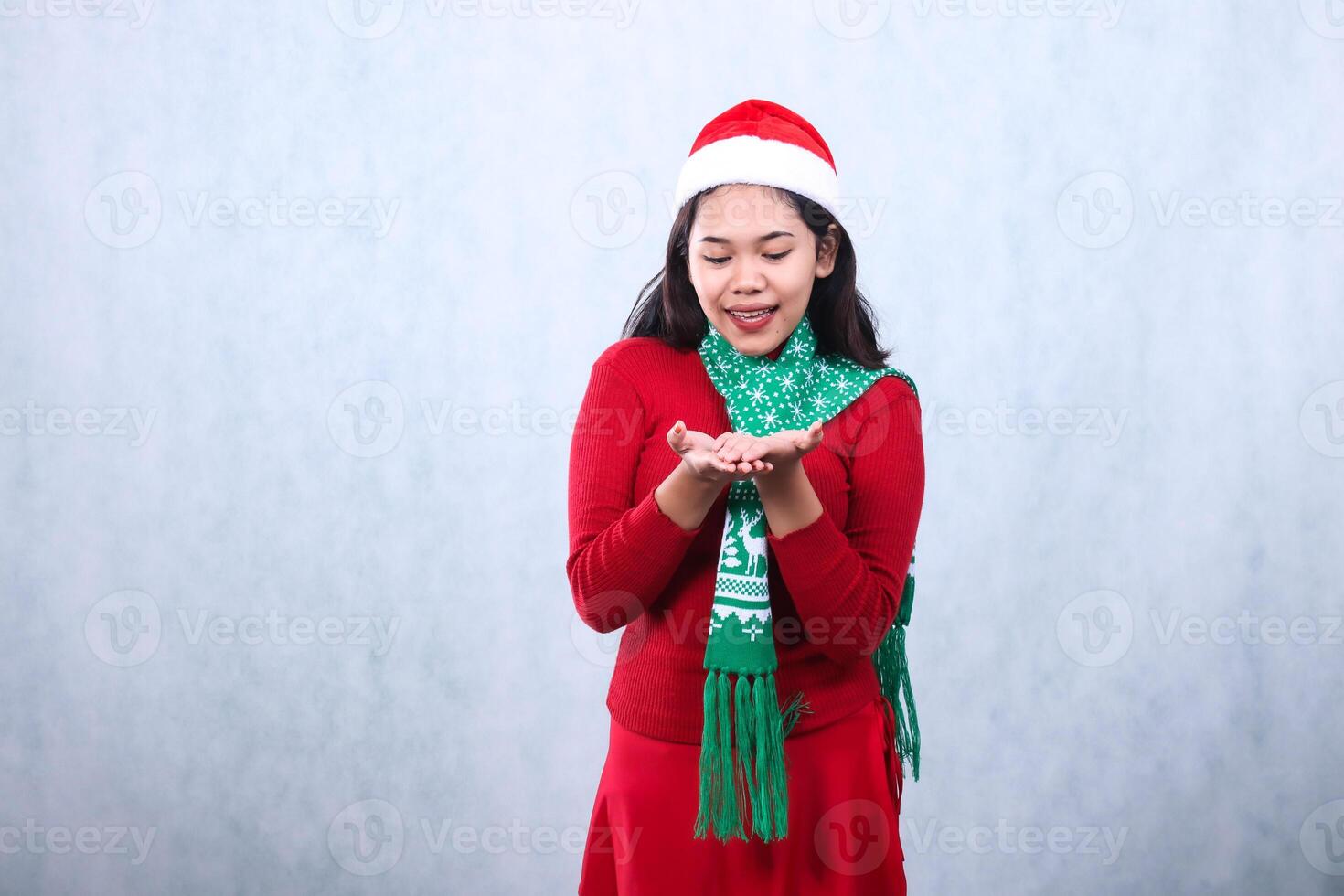 Asian woman gesture wearing red sweater party wear with Santa hat and scarf, smiling to both palms to show off,celebrating christmas and new year isolated on white background photo