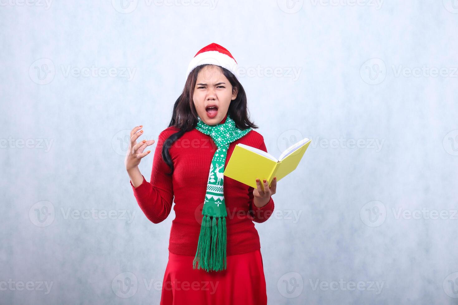 portrait woman wearing red sweater red sweater with Santa hat and scarf celebrating merry christmas,screaming loudly to camera holding book in hand growling stressed ,isolated on white background photo