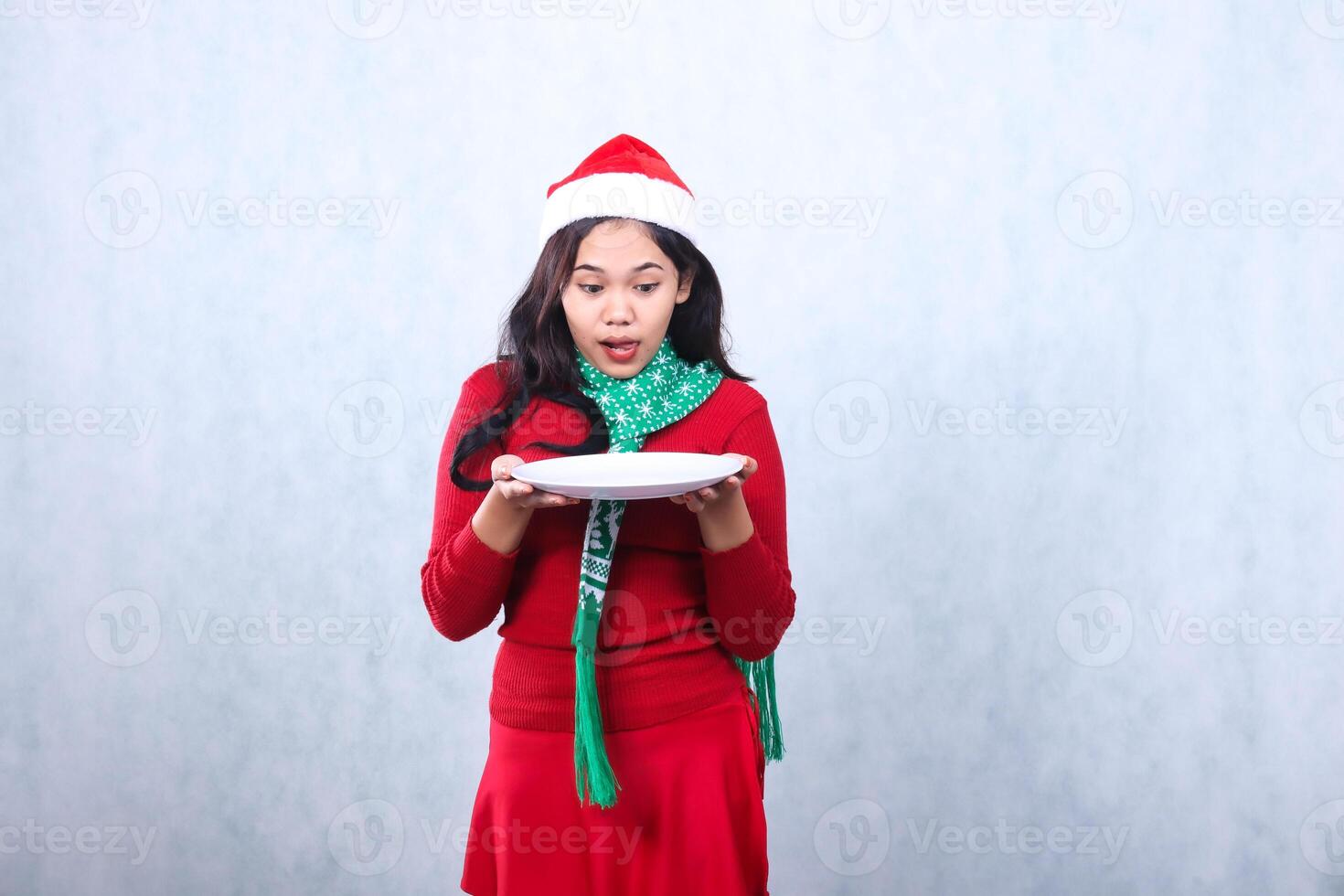 portrait woman wearing red sweater with Santa hat and scarf, focus look at plate both hands hold white plate, celebrate merry christmas and new year isolated on white background photo