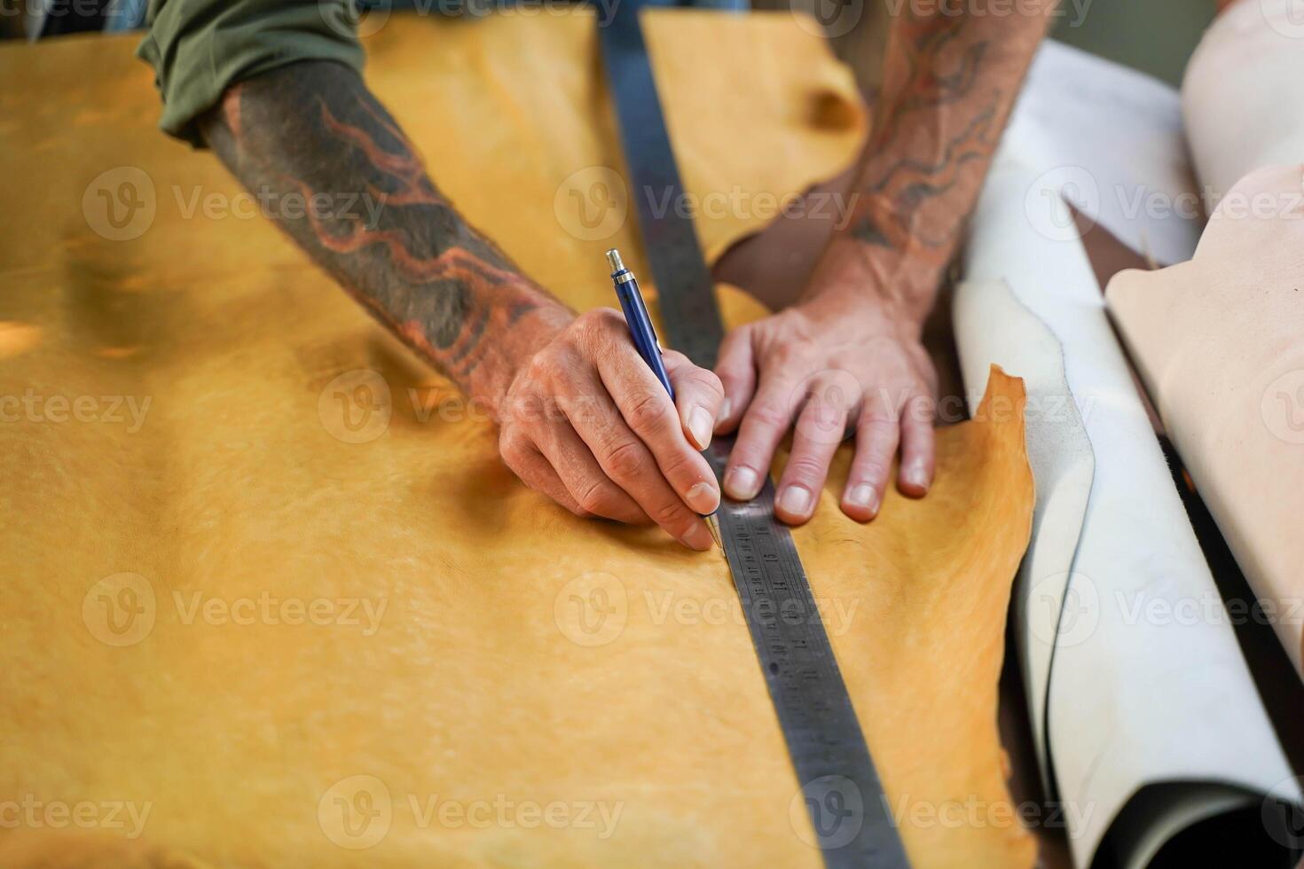 Closeup and crop hands of leather craftsman using a pencil and steel ruler drawing design on the yellow leather in the workshop. photo