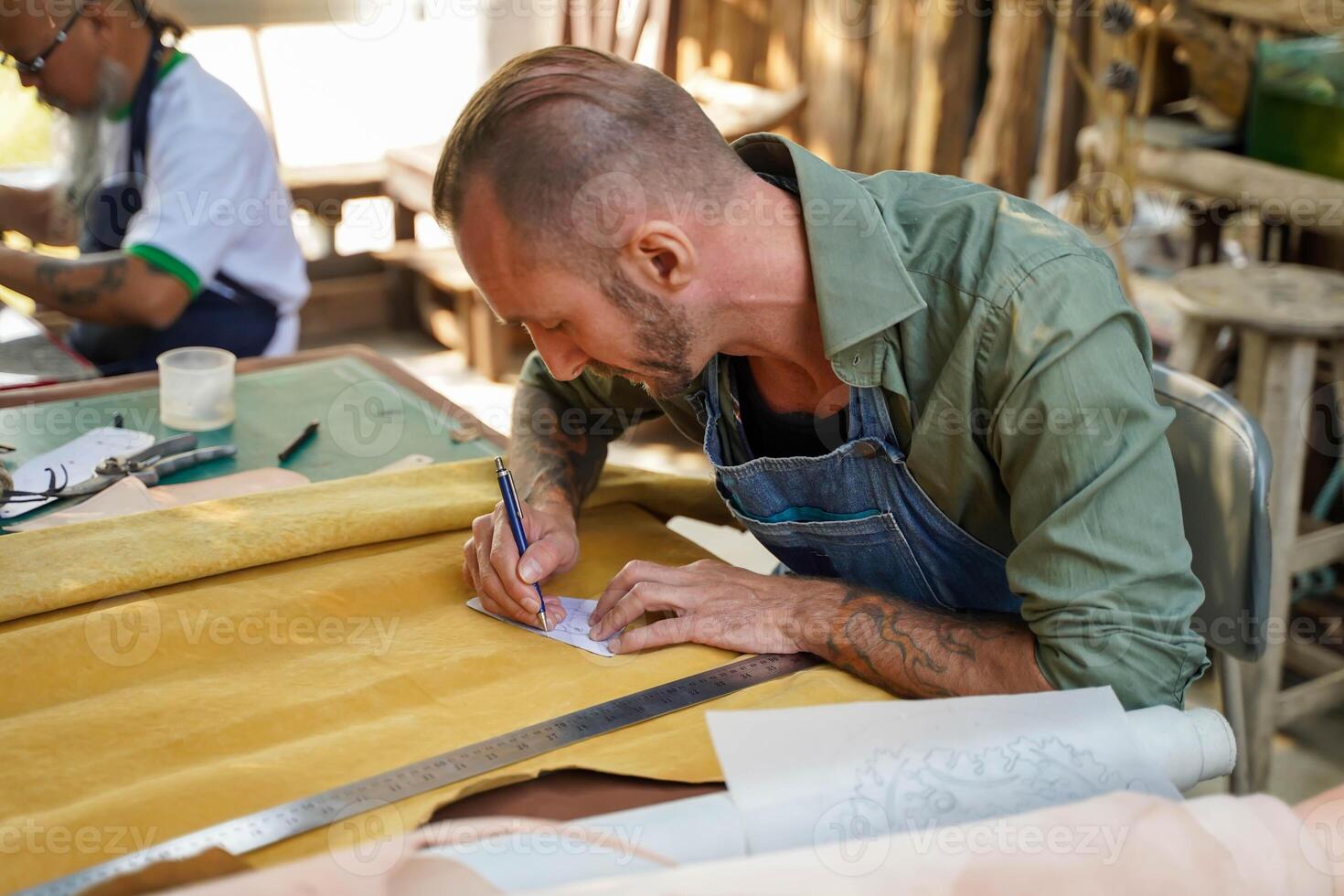 Leather craftsman using a pencil drawing draft design on the yellow leather in the workshop. photo