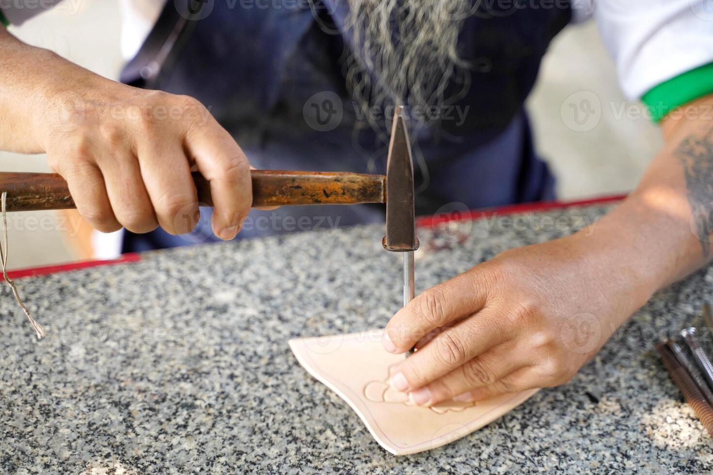 Closeup hands of leather craftsman using a small hammer with carefully to make a leather product for a customer., Leather craftsman concept. photo