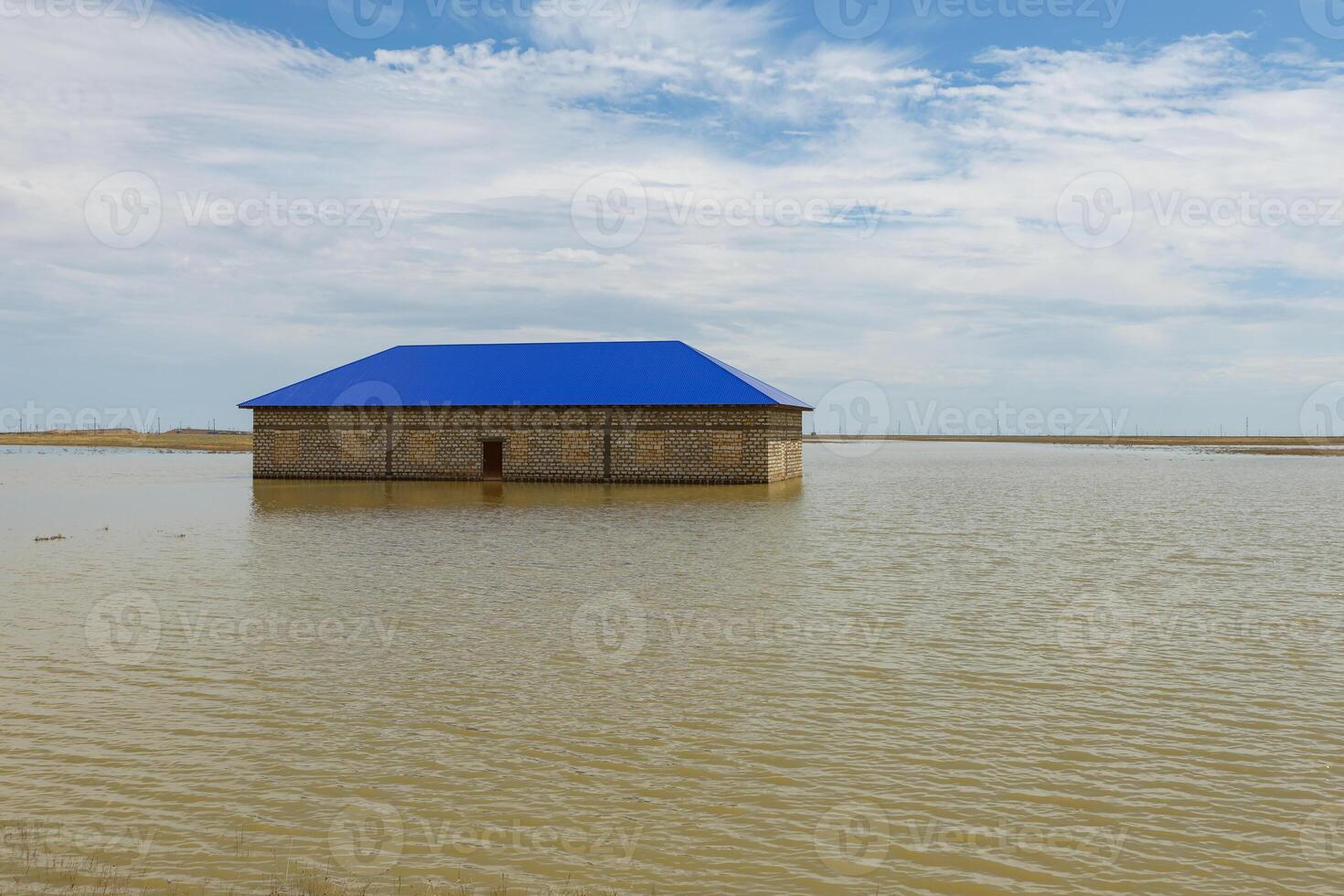 Flooded building with blue roof surrounded by water under a cloudy sky photo