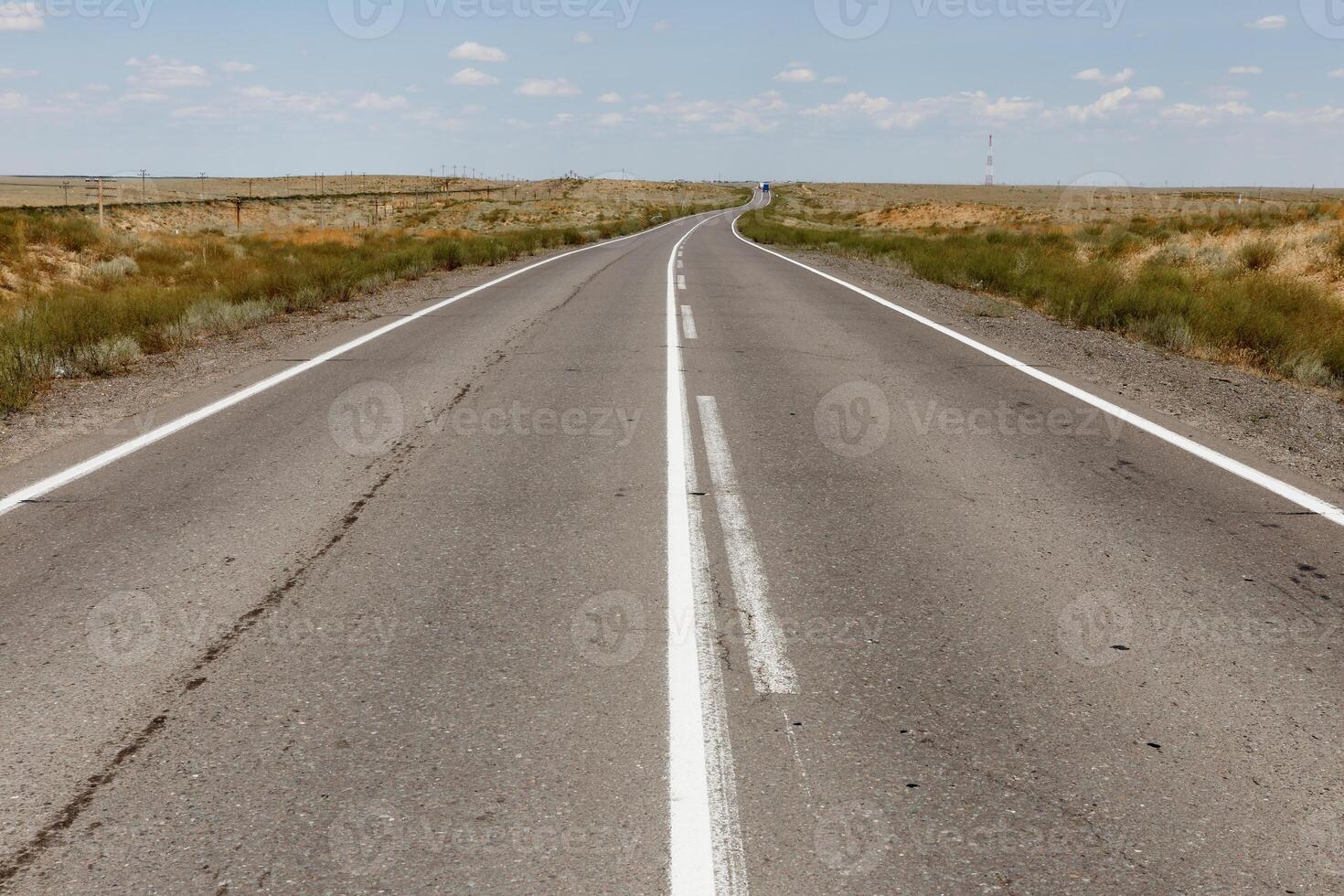 Expansive highway stretching through the scenic landscape of Kazakhstan under a clear sky photo