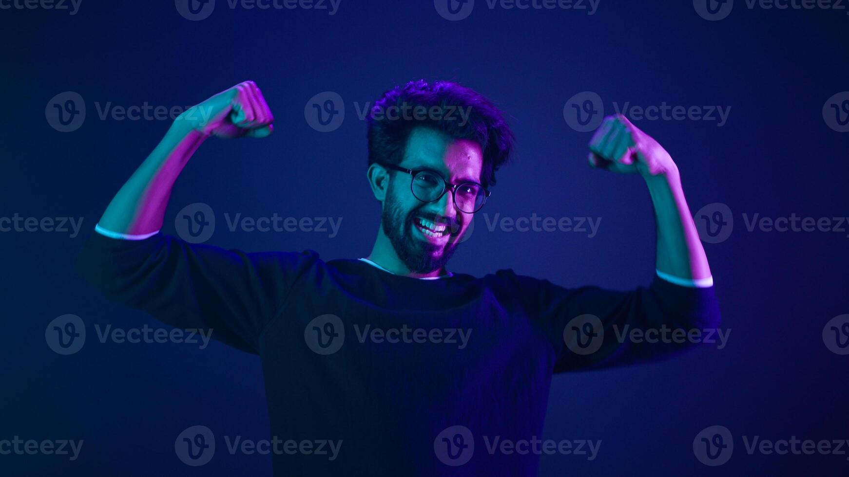Funny Indian man slim guy fooling around show hands muscle biceps sport strong power bodybuilder ultraviolet neon studio background proud champion boast efficient security coding achievement level up photo